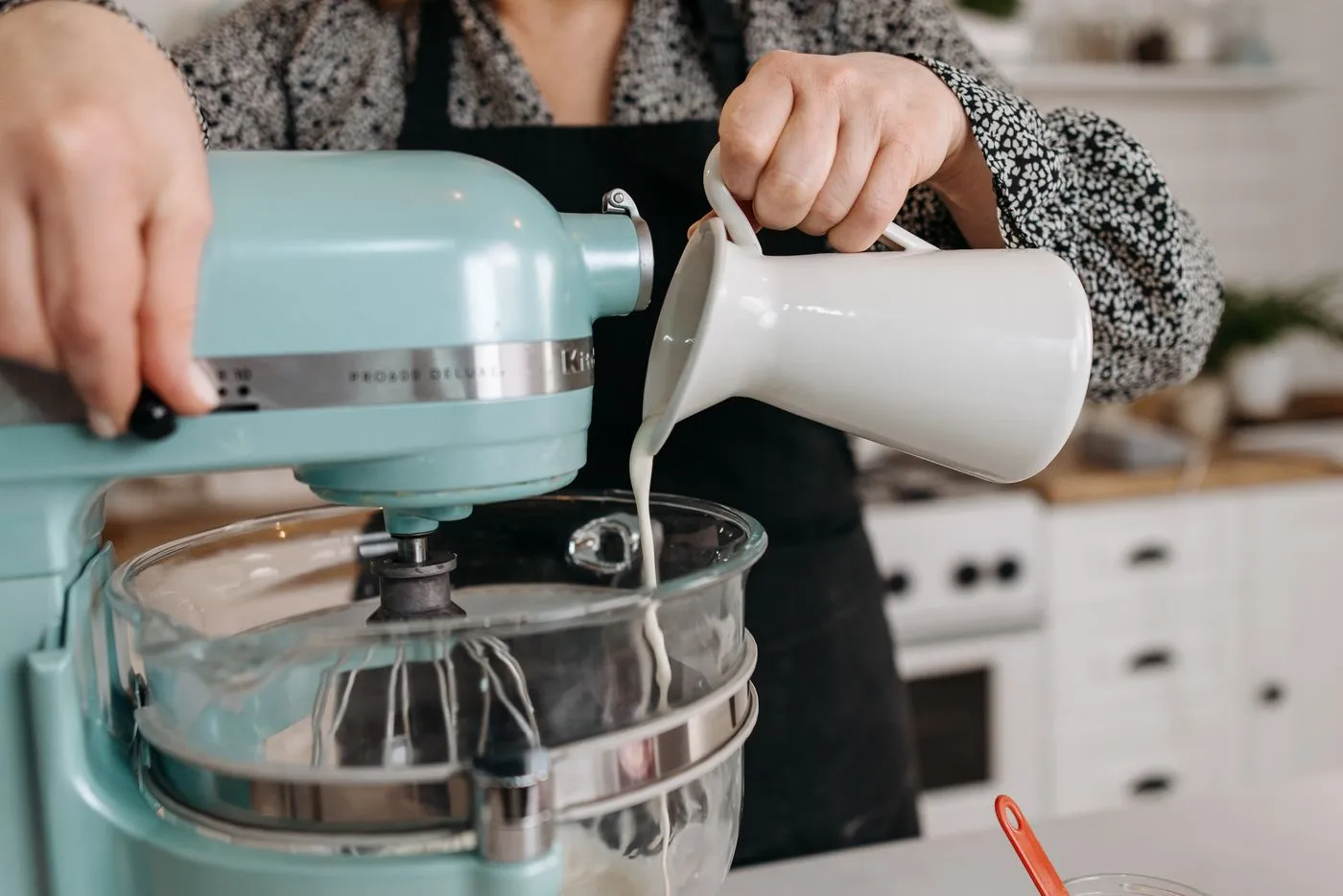 Robot pâtissier KitchenAid turquoise dans lequel on verse du lait, base d'une préparation pour glace